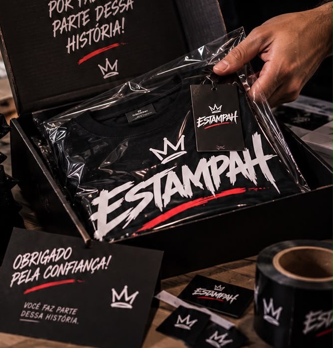 Caixa preta Estampah aberta com camiseta embalada e cartão de agradecimento